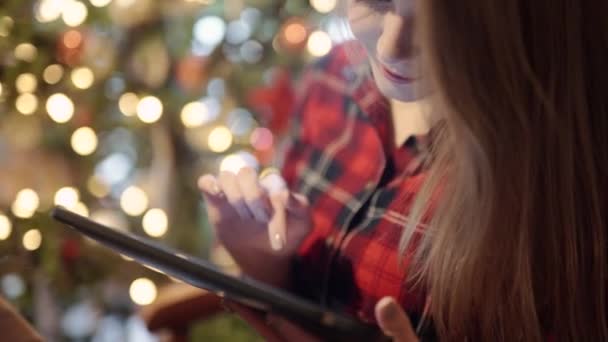 Ευτυχής νεαρή γυναίκα που χρησιμοποιούν tablet pc μπροστά από το χριστουγεννιάτικο δέντρο — Αρχείο Βίντεο