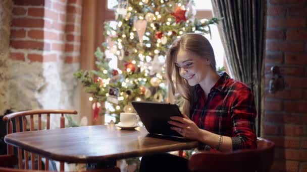 Glad ung kvinna använder TabletPC framför granen — Stockvideo