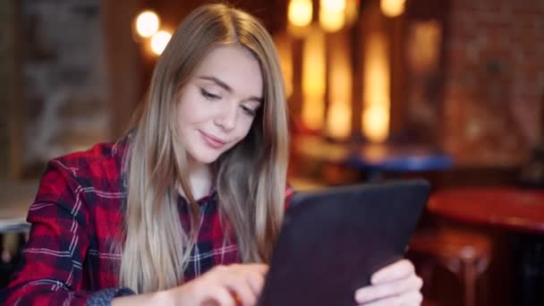Счастливая молодая женщина пьет кофе и пользуется планшетным компьютером в кафе — стоковое видео