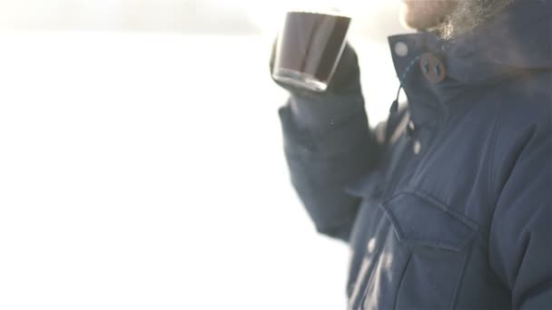 Молодой человек пьет горячий кофе на открытом воздухе в холодный зимний день — стоковое видео