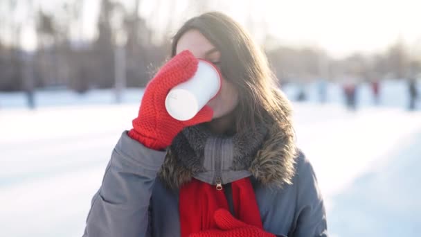 Girl with mug of hot drink on ice skating rink — Stock Video