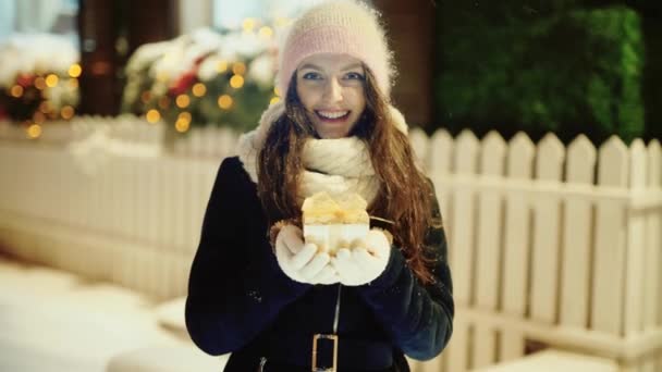 Glad ung kvinna med en liten nuvarande låda i snöig natt — Stockvideo