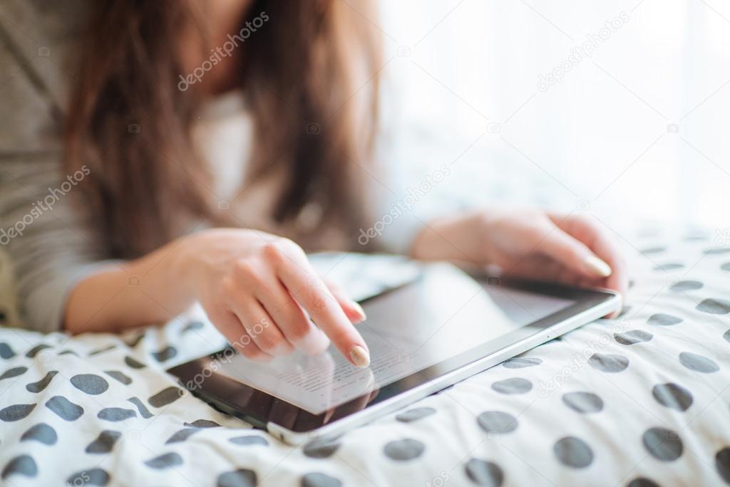 Woman lying in bed with digital tablet touching with finger. View from above