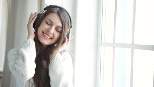 Woman listening music in headphones on windowsill background — Stock Video