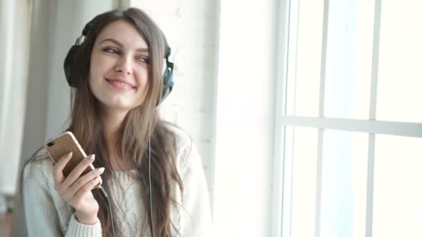 Woman listening music in headphones on windowsill background — Stock Video