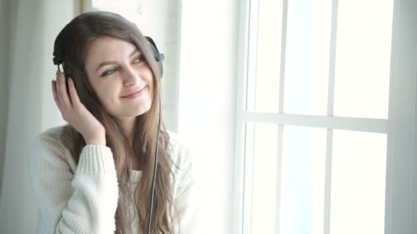 Woman listening music in headphones on windowsill background — Stock Video