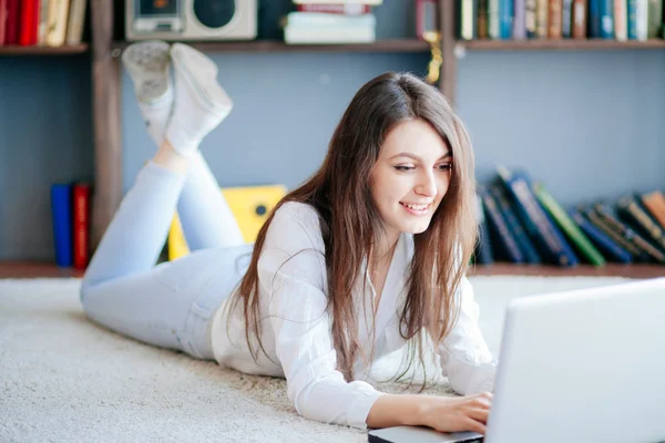 Evde dizüstü bilgisayar kullanan mutlu genç bir kadın.