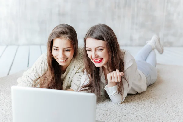 Dos mujeres felices mirando a la computadora portátil mientras yacen en el suelo — Foto de Stock