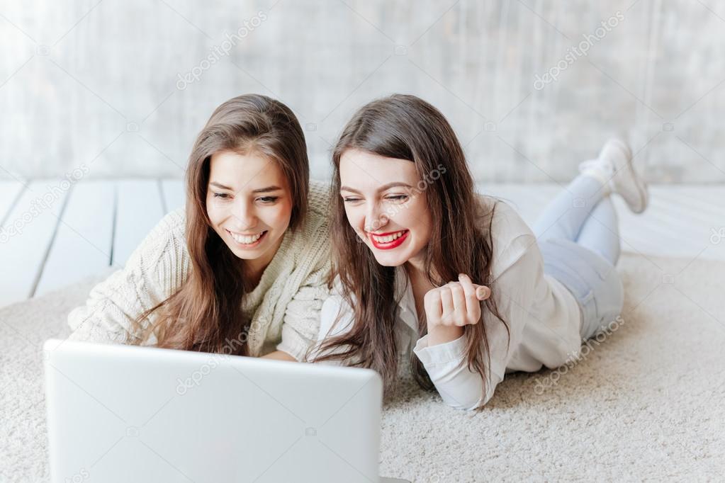 Two Happy Women Looking At Laptop While Lying On Floor