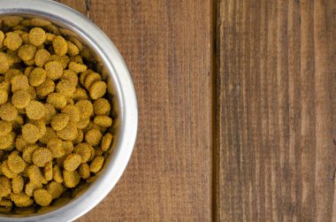 Ahşap arka planda metal kasede kuru kedi maması. Fotoğraf.