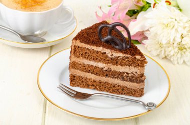 Bir parça çikolatalı pasta, kapuçino, masada çiçekler. Stüdyo Fotoğrafı