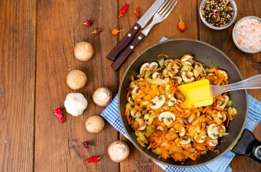 Kızarmış mantarlı tava şampiyonlar, soğanlar ve havuçlar ahşap arka planda..