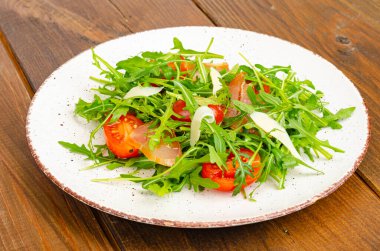 Bir tabak roka, domates, kurutulmuş et ve peynir. Ahşap arka planda tabakta salata. Stüdyo Fotoğrafı