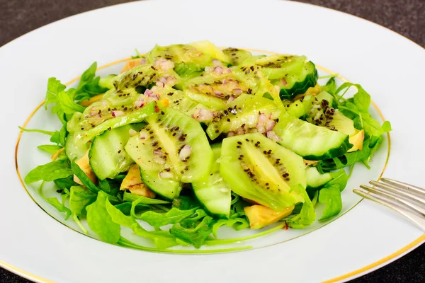 Arugula salad, kiwi and cucumber on white plate
