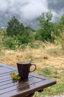 Bulutlu bir yaz gününde, dağların arka planında, ahşap bir masanın üzerinde kahve fincanı.