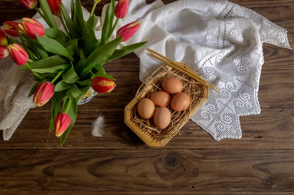 The easter composition. Eggs, a red tulips and church candles on wooden table close-up.