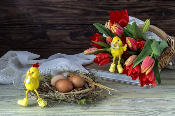 The easter composition. Eggs, a red tulips, toys and church candles on wooden table close-up.
