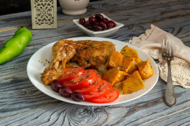 Haşlanmış tavuk budu, tatlı patatesler (Ipomoea batatas), domatesler ve zeytinler ahşap bir masada yakın plan beyaz bir tabakta uzanır.