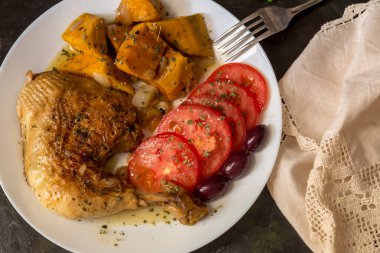 Haşlanmış tavuk budu, tatlı patatesler (Ipomoea batatas), domatesler ve zeytinler ahşap bir masada yakın plan beyaz bir tabakta uzanır.