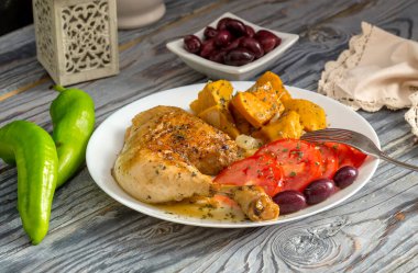 Haşlanmış tavuk budu, tatlı patatesler (Ipomoea batatas), domatesler ve zeytinler ahşap bir masada yakın plan beyaz bir tabakta uzanır.