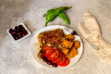 Haşlanmış tavuk budu, tatlı patatesler (Ipomoea batatas), domatesler ve zeytinler ahşap bir masada yakın plan beyaz bir tabakta uzanır.