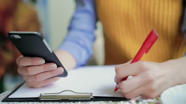 Ręczne pisanie i trzymając telefon w tabeli. Powiększenie — Wideo stockowe