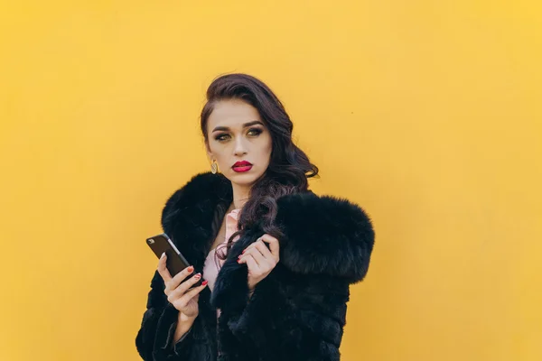 Menina bonita com o telefone em um fundo amarelo — Fotografia de Stock