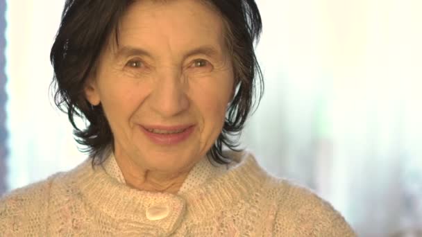 Retrato de una anciana feliz sonriendo en una cámara sobre un fondo brillante. Despacio. — Vídeos de Stock