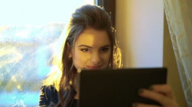 Tablet bir pencere ve perdeleri arka planı kullanma ve gülümseyen kadın