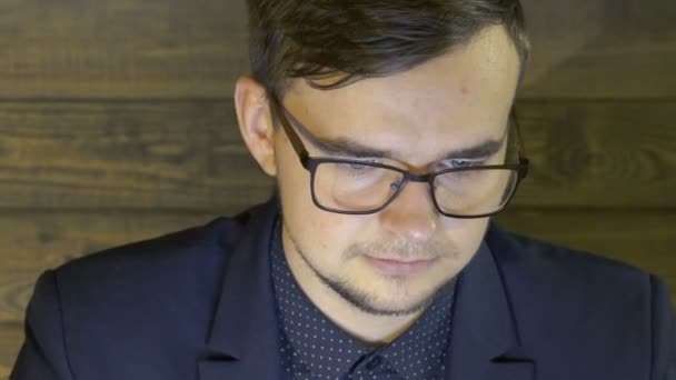 Чоловік в окулярах працює з ноутбуком на фоні дерев'яної стіни — стокове відео