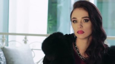 Bayan kürk oturan, kameraya bakıyor ve gülümsüyor. Yavaş yavaş