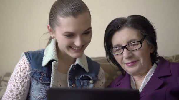 Девушка и старуха с помощью планшета на диване, улыбаясь, заботясь — стоковое видео