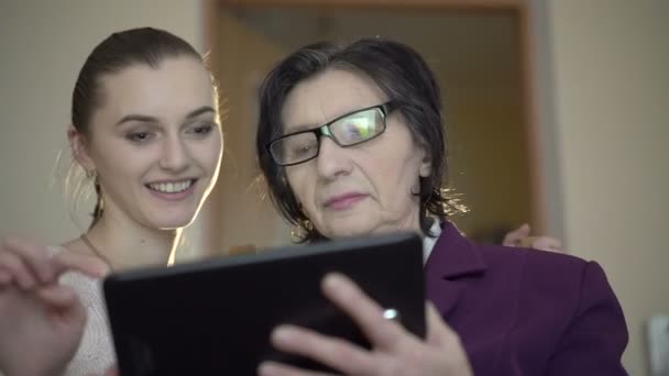 Elegante oude zakelijke vrouw en jonge meisje met een tablet op de achtergrond van de kamer — Stockvideo