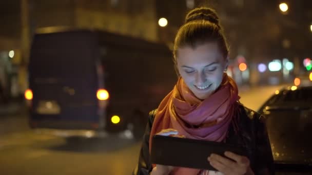 Menina bonita sorrindo, usando tablet à noite na rua. 4K — Vídeo de Stock