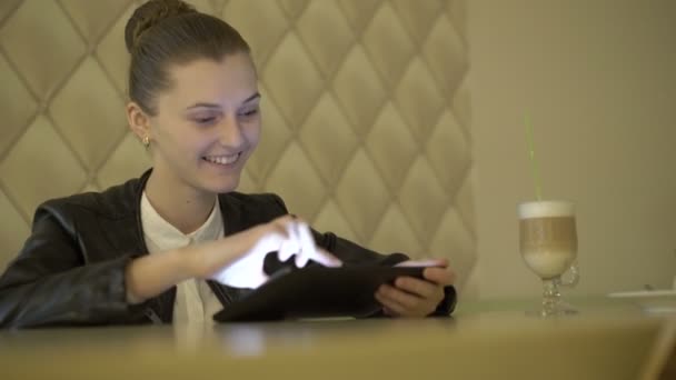 Chica alegre usando una tableta, sonriendo en la cafetería. 4K — Vídeos de Stock