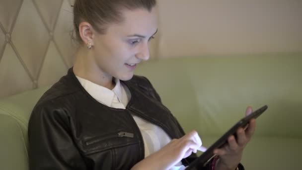 Rubia alegre sentada en el sofá y usando la tableta. 4K — Vídeos de Stock