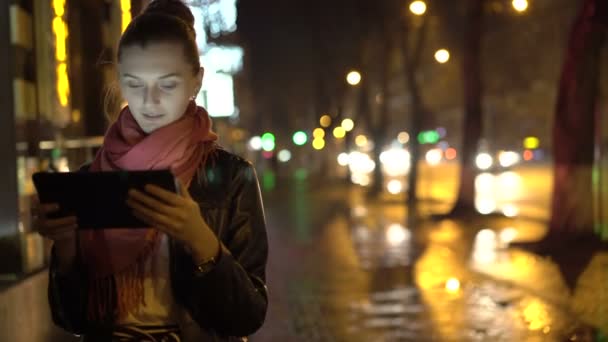 女孩站在人行道上，在晚上使用平板电脑。4 k — 图库视频影像