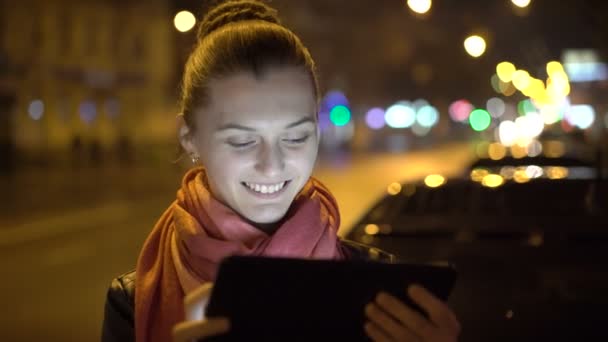 性格开朗的女孩，微笑着，街上晚上按时使用平板电脑。4 k — 图库视频影像