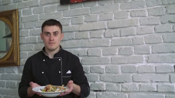 Chef en uniforme negro presenta ensalada de sabor sobre fondo de pared de ladrillo blanco 4k — Vídeos de Stock