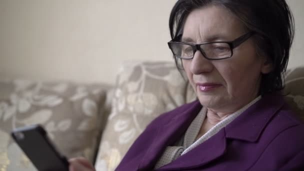 Olgun kadının portresi smartphone bir kanepe arka plan üzerinde kullanarak yakın çekim — Stok video
