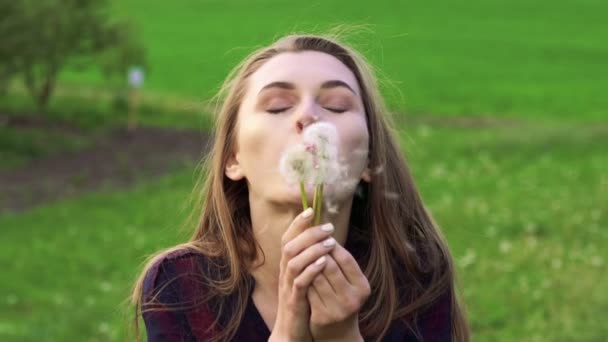 Mujer joven y bonita soplando diente de león y sonriendo. Movimiento lento — Vídeos de Stock