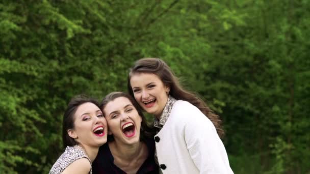 Три девушки в объятиях улыбаются и смотрят в камеру. Медленно. — стоковое видео