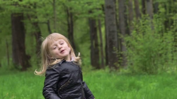Jolie petite fille debout, marchant sur une caméra et souriant dans un parc. Doucement. 