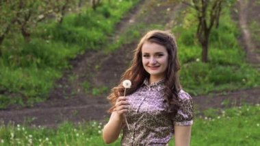 Genç model bahçede karahindiba üfleme ve gülümseyerek. Yavaş yavaş