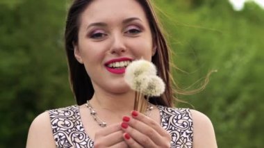 Karahindiba üfleme ve bir kameraya gülümseyen esmer. Ağır çekim