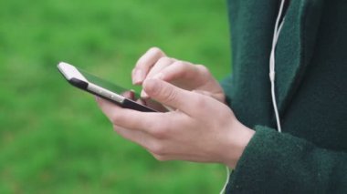 Çim zemin 4 k üzerinde kulaklık ile telefon kullanarak kadın el yakın çekim