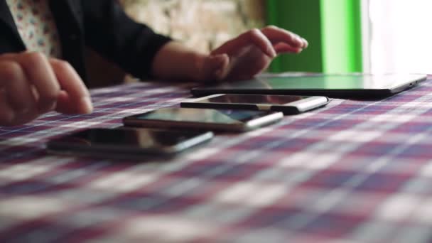 Manos de mujer trabajando con una tableta cerca de tres teléfonos en una mesa en la cafetería 4k — Vídeos de Stock