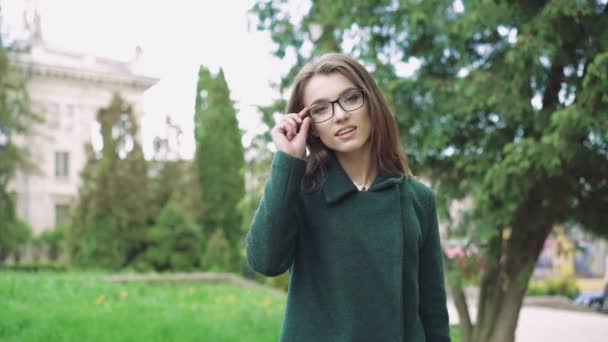 Молодая девушка позирует перед камерой в пальто на фоне дерева 4k — стоковое видео
