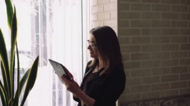 Bir pencere ve günbatımı arka plan üzerinde bir tablet kullanan iş kız. 4k