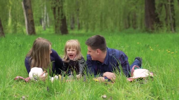 Glückliche Eltern mit Baby auf dem grünen Gras liegend und küssend. langsam — Stockvideo
